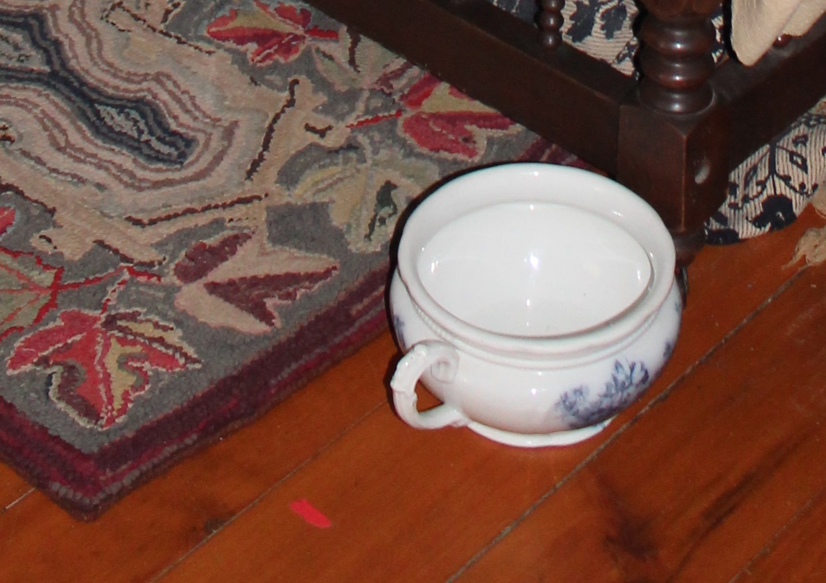 chamber pot sits at the foot of a bed