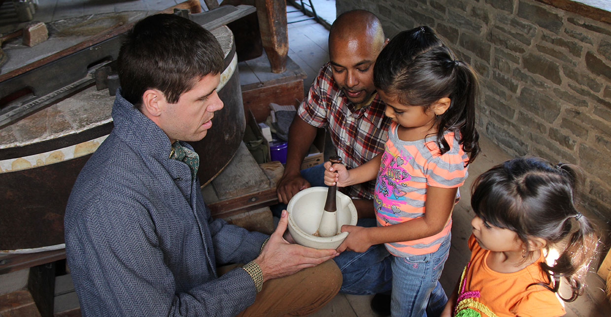 a Black Creek interpreter shows a young visitor how to grind grain in a mortar