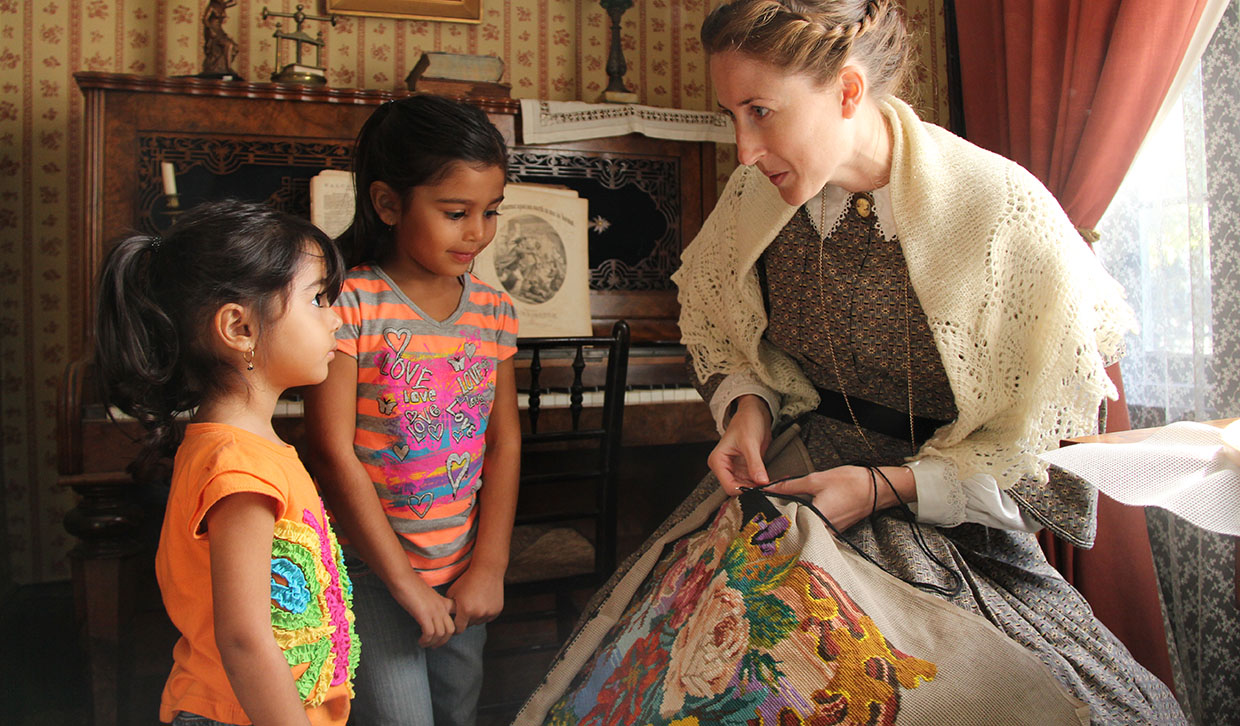 a Black Creek interpreter demonstrates needlepoint for two young visitors