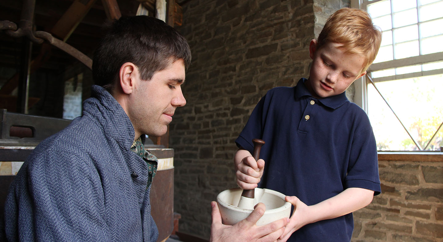 a young visitor to Black Creek practices crushing grain with a pestle