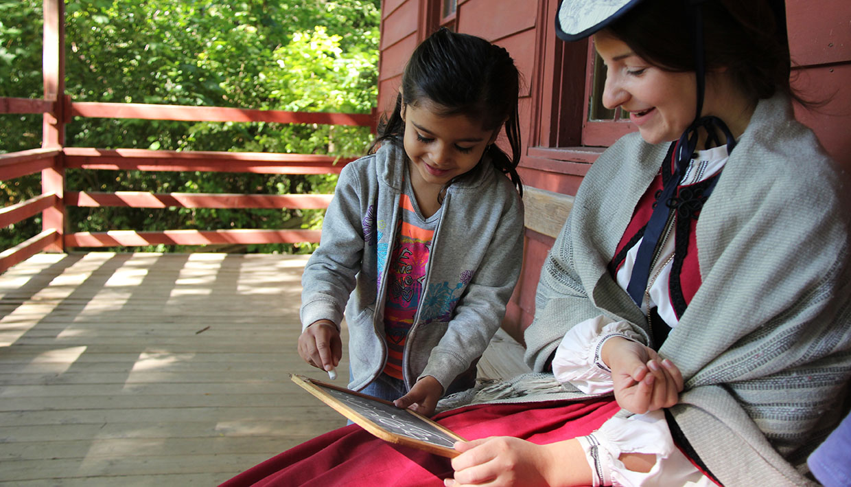 a young visitor to Black Creek practices writing on a slate
