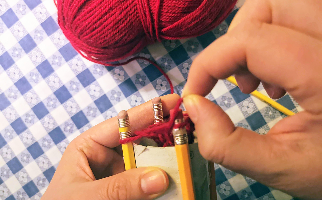 crafter casts on by passing bottom loop of yarn over top loop