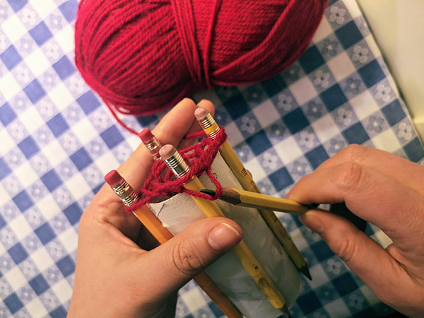 crafter wraps yarn around outside of pegs