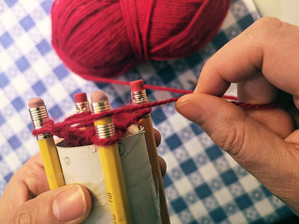 crafter wraps yarn around outside of pegs