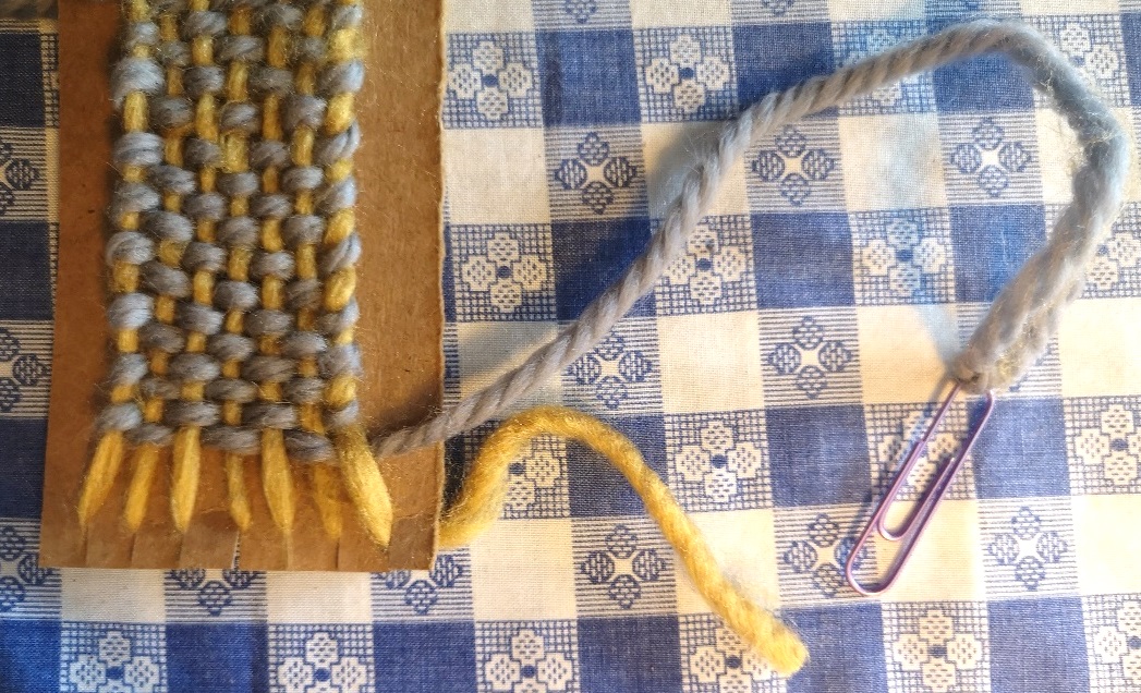 a crafter uses cardboard and yarn to make a woven bookmark