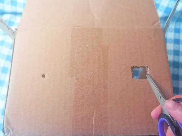 crafter uses scissors to add viewing hole to camera obscura