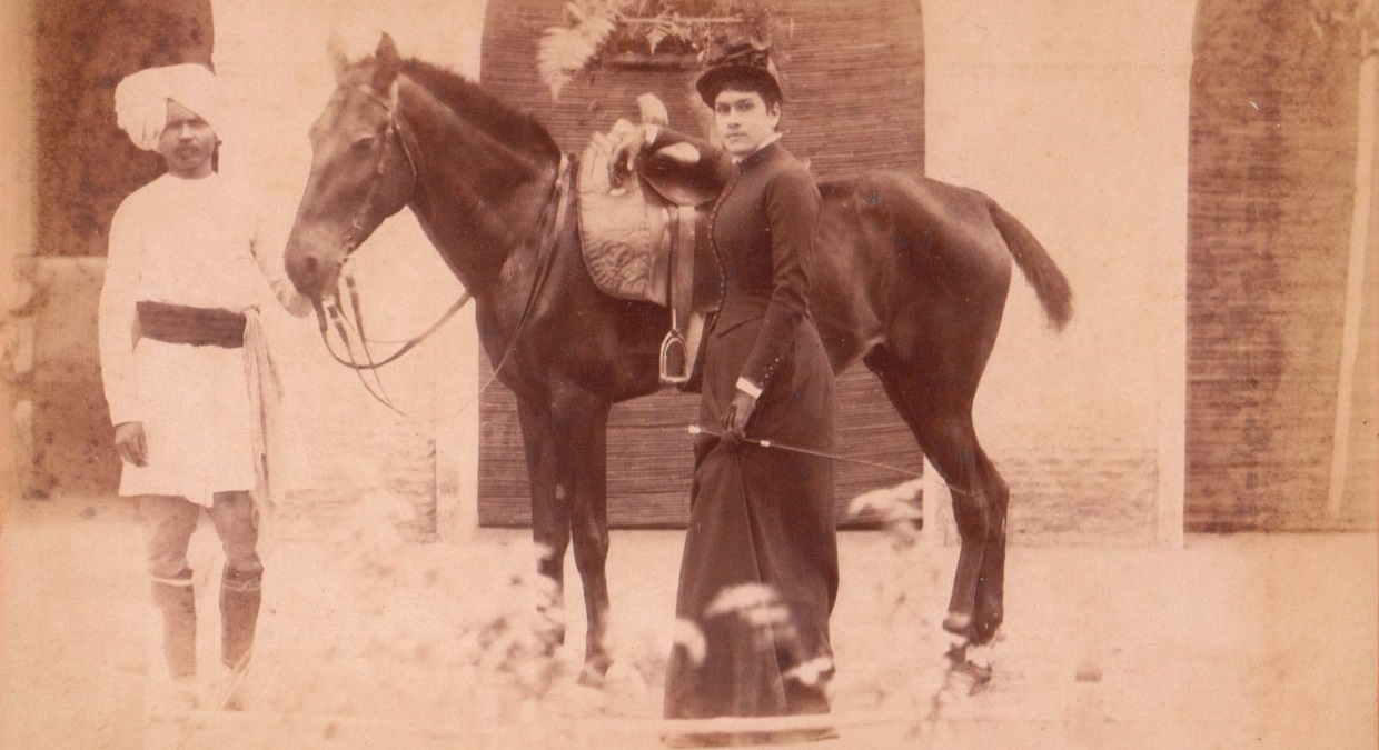 woman wearing side saddle habit stands next to groom wearing jodhpurs