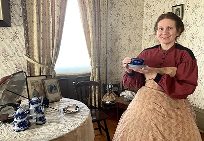 Victorian woman wearing hoop skirt enjoys cup of tea in the parlour