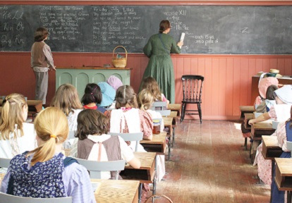 teacher leads class in one-room 19th century rural schoolhouse