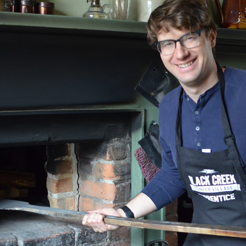 corporate team member uses wood burning oven to prepare baked good as part of bake off challenge at Black Creek Pioneer Village