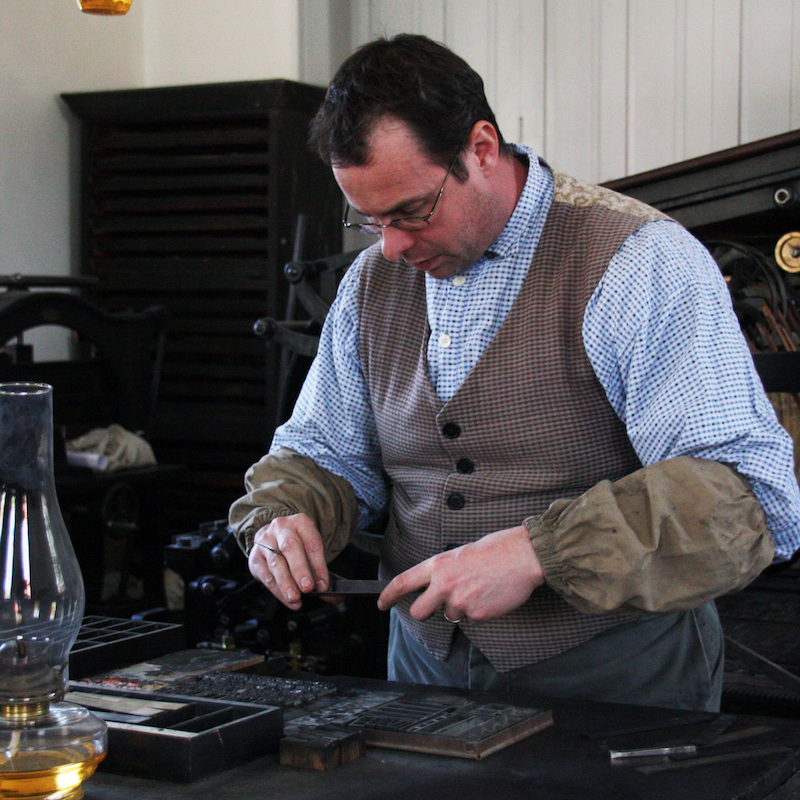 costumed educator demonstrates the 19th century method of setting type at the Black Creek Pioneer Village printers office