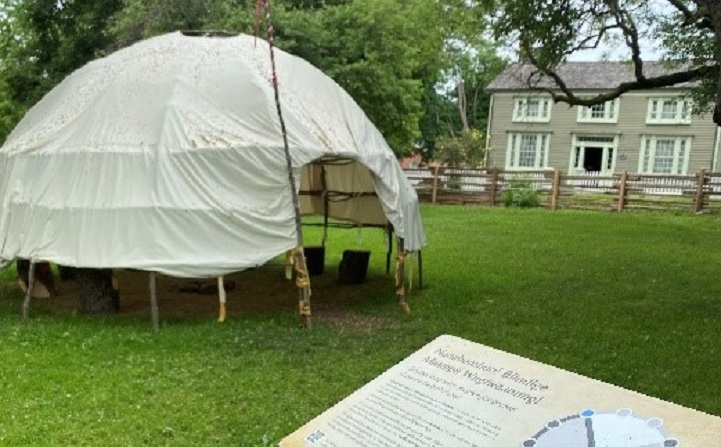 a wiigiwaam accompanied by an informational panel at the Village at Black Creek