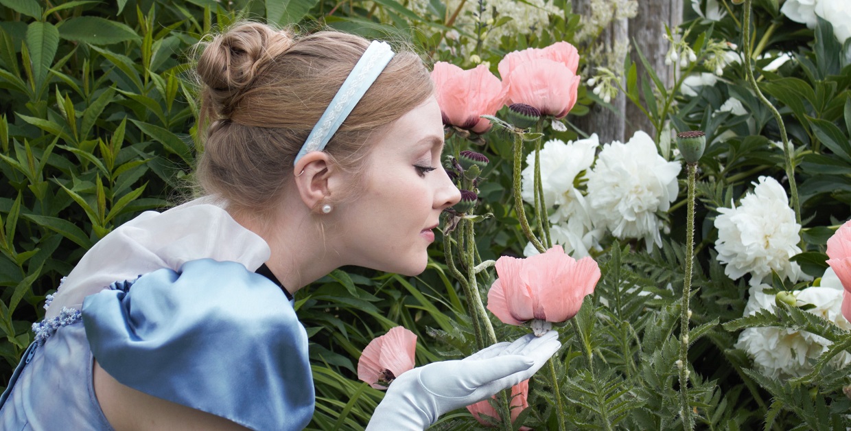 a history actor in a fairy tale princess costume stops to smell the roses growing in a garden at Black Creek Pioneer Village