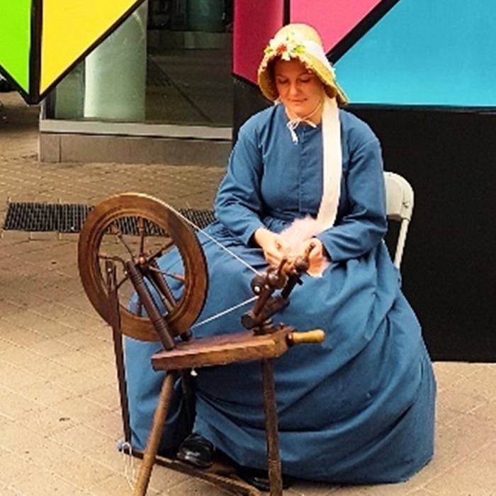 a costumed historian from Black Creek Village demonstrates an old-fashioned spinning wheel at a local community event