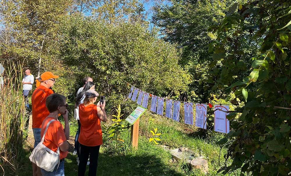 A group of people wearing orange t-shirts standing in a line with paper signs on a trail